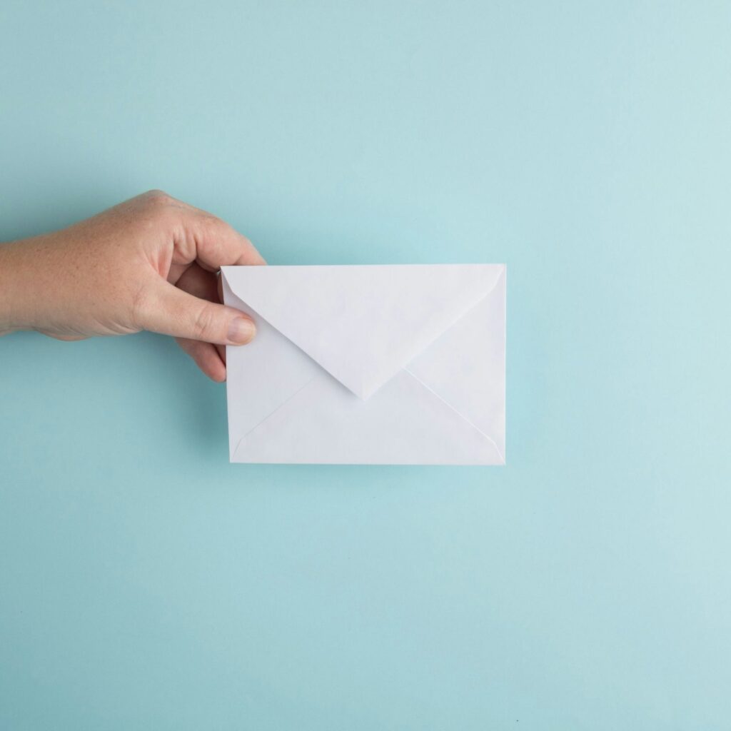 Hand holding a plain white envelope against a light blue background