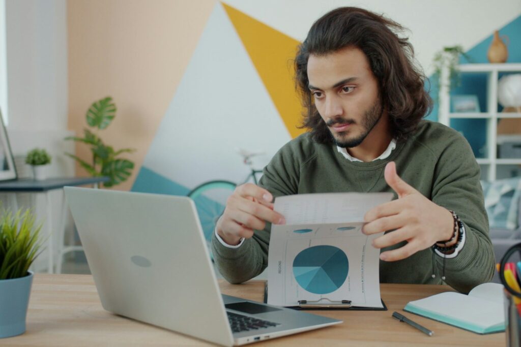 Small business owner reviewing paperwork at a laptop in a bright office